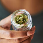 african american woman opening bottle of legal marijuana from dispensary close up with selective focus on weed