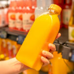 Person holding a bottle of orange juice in a supermarket